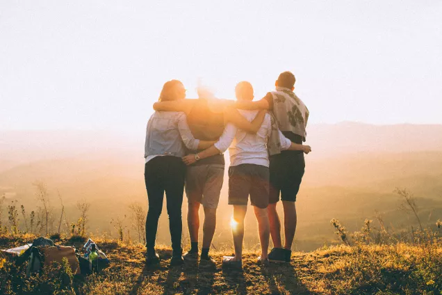 Four people standing side by side towards sunset. Photo.