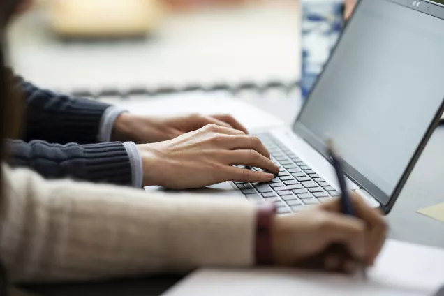 The image shows a laptop and hands typing on it