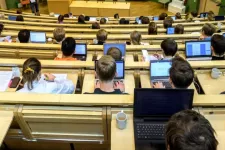 Students with computers in big hearing room.