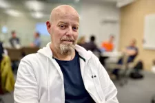 Magnus Hillman has a beard, wears a dark blue t-shirt and a white hoodie