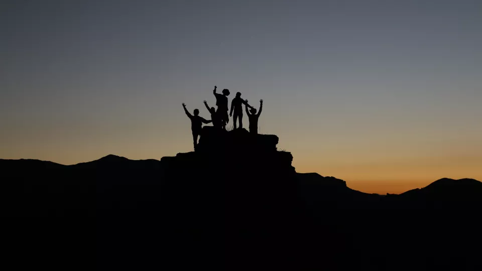 Siluett av en grupp människor som tillsammans bestigit ett berg. Foto.