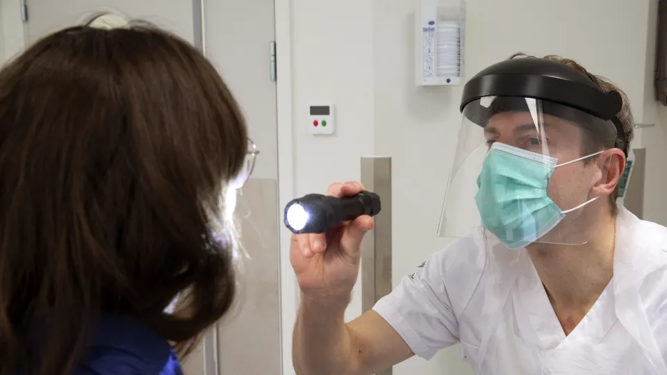 Carl-Johan Fraenkel undersöker en patient med ficklampa iförd visir och munskydd.