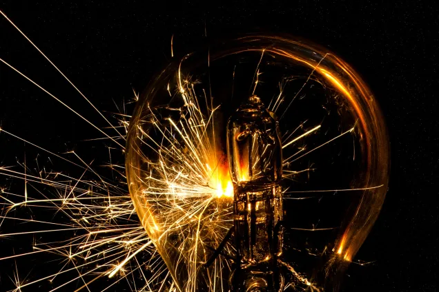 Bilden visar en glödlampa i mörkret med glöd som sprakar från den.