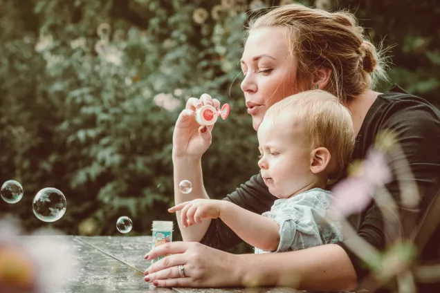 Kvinna med barn i famnen, blåser såpbubblor. Foto.
