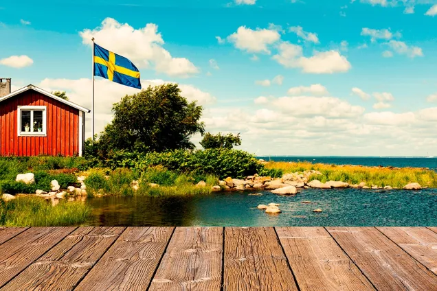Bild av skärgårdsmiljö, röd stuga med vita knutar. 
