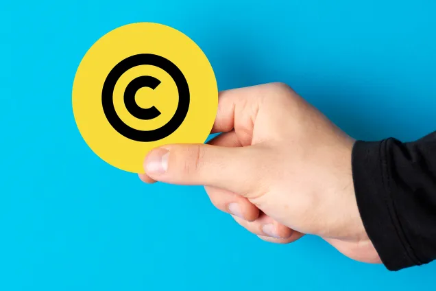 Hand håller ett runt, gult kort med symbolen för upphovsrätt. Fotokollage.